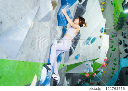 Asian sportswoman practices an indoor rock climbing wall. Asian sportswoman practices an indoor rock climbing wall. 121793256