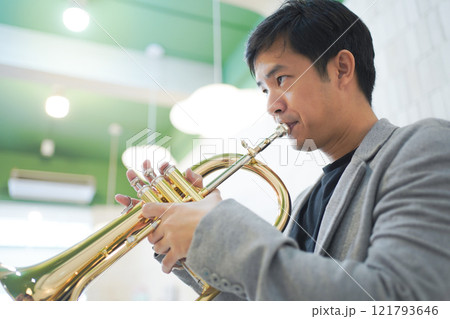 Asian man plays cornet. A solo Asian skillful musician is playing or practicing cornet in the restaurant. A man enjoy playing cornet or trumpet. 121793646