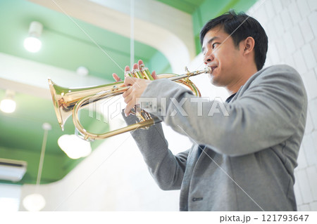 Asian man plays cornet. A solo Asian skillful musician is playing or practicing cornet in the restaurant. A man enjoy playing cornet or trumpet. 121793647