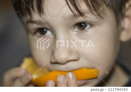 A little boy is eating a slice of orange, close-up. A little boy is eating a slice of orange, close-up. 121794393