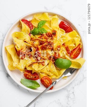 Tagliatelle or pappardelle pasta with tomato sauce, basil and parmesan cheese in a plate with fork 121794879