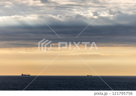 The sun sets over a peaceful sea, with distant ships, creating a serene maritime view The sun sets over a peaceful sea, with distant ships, creating a serene maritime view 121795756