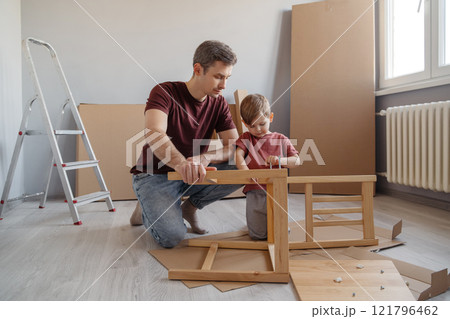 A young boy assists his dad in assembling furniture at home 121796462
