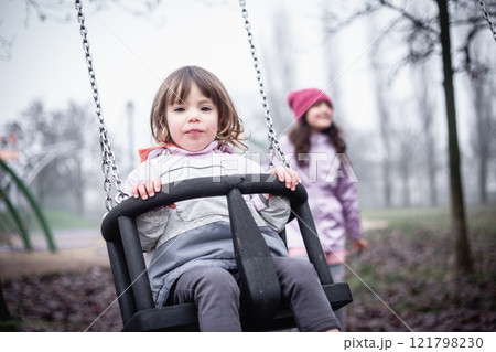 one small child sitting on the swing at children playground on a foggy day, playing with other child one small child sitting on the swing at children playground on a foggy day, playing with other child 121798230