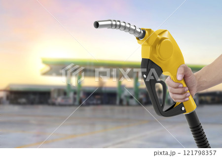 Holding a fuel nozzle against with gas station blurred background Holding a fuel nozzle against with gas station blurred background 121798357