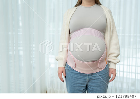 Pregnant woman adjusting a supportive maternity belt, copy space. Orthopedic abdominal support waist, back, abdomen band. Belly brace for pregnancy.Comfort, and essential care during pregnancy Pregnant woman adjusting a supportive maternity belt, copy space. Orthopedic abdominal support waist, back, abdomen band. Belly brace for pregnancy.Comfort, and essential care during pregnancy 121798407