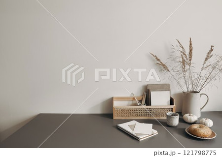 Modern summer, fall still life photo. Grey ceramic vase with dry festuca grass on old wooden stool. White wall background. Empty copy space. Elegant lifestyle decorative scene. Trendy interior decor. 121798775