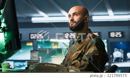 Special forces professional in military HQ base gathering information on enemy troops. Officer using monitoring equipment in base of operations to do assessment of enemy vulnerabilities, camera A 121799573