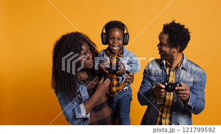 Joyful optimistic dad playing online video games with his boy using controller, parents enjoying leisure time with their small child. African american happy family play together in studio. Camera B. Joyful optimistic dad playing online video games with his boy using controller, parents enjoying leisure time with their small child. African american happy family play together in studio. Camera B. 121799592