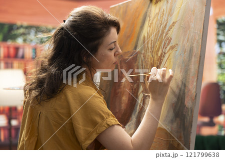 Inspired artist works on a canvas to create a masterpiece in atelier, using bristles to apply dye with precision. Showing her skill during creative process to create unique painting for the gallery. Inspired artist works on a canvas to create a masterpiece in atelier, using bristles to apply dye with precision. Showing her skill during creative process to create unique painting for the gallery. 121799638