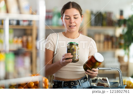 Young woman chooses pickled cucumbers and tomatoes 121802761