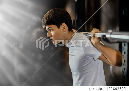 Slender guy trains muscles of arms and back using barbell and differentiated weighting in gym Slender guy trains muscles of arms and back using barbell and differentiated weighting in gym 121802765