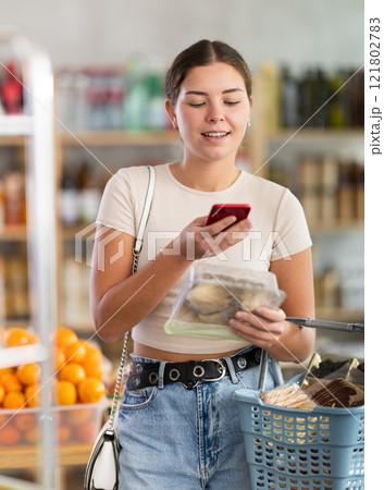 Girl inspects oyster mushrooms, photographs QR code on label by smartphone 121802783