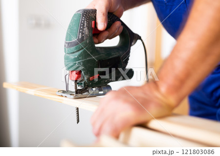 Work with an electric jigsaw - cutting wooden board close-up Work with an electric jigsaw - cutting wooden board close-up 121803086