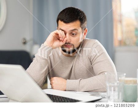 Man rubs tired eyes with his hands after a long work at laptop at home Man rubs tired eyes with his hands after a long work at laptop at home 121803209