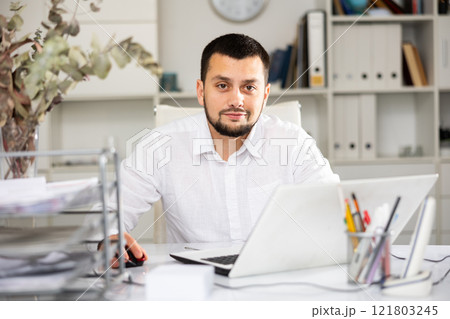 Positive man office worker using laptop during workday Positive man office worker using laptop during workday 121803245