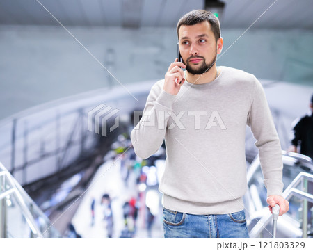 Guy with suitcase talking on phone near escalator at subway station 121803329