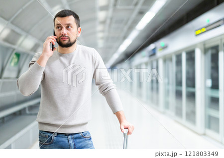 Man with luggage talking on mobile phone at the station in subway Man with luggage talking on mobile phone at the station in subway 121803349