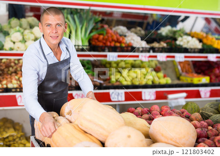 Smiling greengrocery owner laying out fruits and vegetables on counter Smiling greengrocery owner laying out fruits and vegetables on counter 121803402