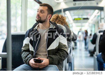 Portrait of european man standing in tram carriage and using phone 121803413