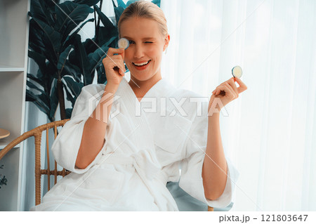 Woman holding slices of fresh cucumber and wearing bathrobe. Quiescent Woman holding slices of fresh cucumber and wearing bathrobe. Quiescent 121803647