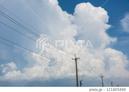 View of utility poles with blue sky and white clouds as a background. 121805898