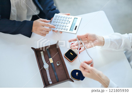 貴金属を査定する買取専門業者とミドル女性の手元 貴金属を査定する買取専門業者とミドル女性の手元 121805930