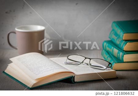 The atmosphere of privacy. On the desk is a stack of books, glasses and an open book. In the background is a mug of tea 121806632