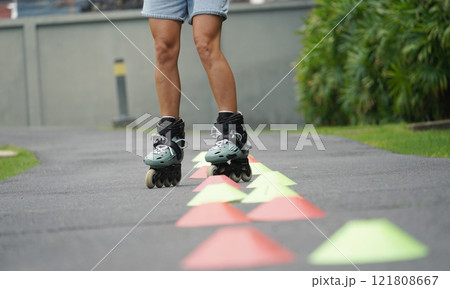 A woman is rollerblading gracefully on a road located in a park 121808667