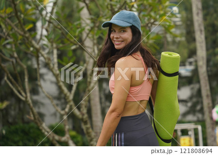 A young woman happily prepares to do yoga on a mat in a beautiful park. A young woman happily prepares to do yoga on a mat in a beautiful park. 121808694