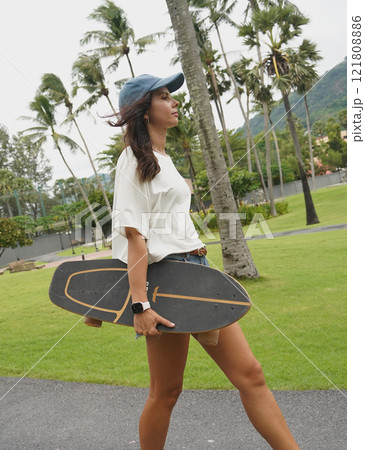 A woman is walking at the city park while carrying a skateboard in her hands 121808886