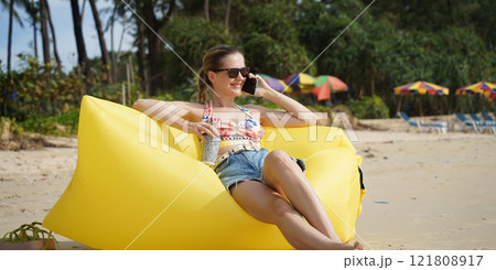 A young woman on the beach lounging on a yellow bean bag A young woman on the beach lounging on a yellow bean bag 121808917