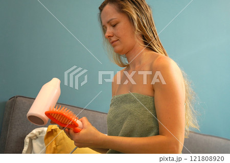 A woman is expertly styling her hair using a blow dryer and brush while in the bathroom 121808920