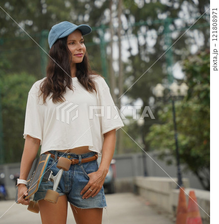 A woman is walking at the city park while carrying a skateboard in her hands 121808971