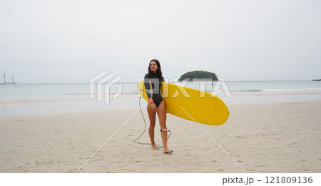 Young woman wearing tight wetsuit is going to surfboard at beautiful beach 121809136
