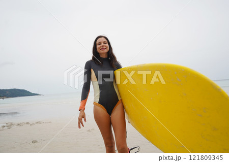 Young woman wearing tight wetsuit is going to surfboard at beautiful beach 121809345