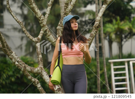 A young woman happily prepares to do yoga on a mat in a beautiful park. 121809545
