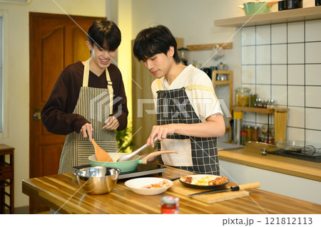 Happy gay couple preparing a delicious meal together in bright and cozy kitchen Happy gay couple preparing a delicious meal together in bright and cozy kitchen 121812113