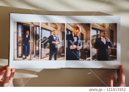 Female hands flipping through a photo book with wedding photos on a white table 121813952
