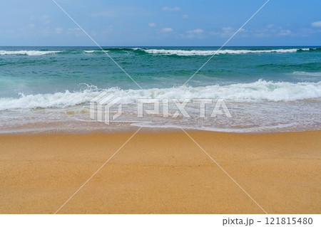 Sandy beach with turquoise ocean waves in background under blue sky 121815480