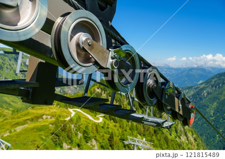 Impressive Black Cable Car Wheel Overlooking Lush Green Mountains and Scenic Landscape Views Impressive Black Cable Car Wheel Overlooking Lush Green Mountains and Scenic Landscape Views 121815489