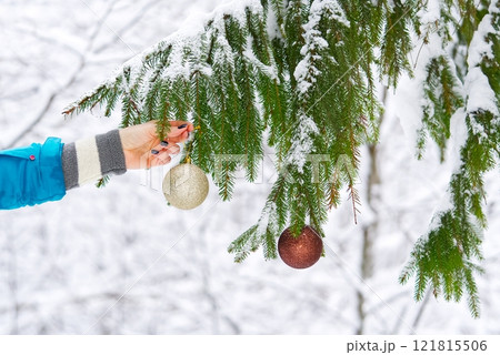 Happy Woman Hanging a Beautiful Golden Christmas Ball on a Snowy Fir Tree Outside 121815506