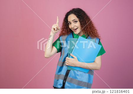 Front view of happy, pretty woman with red, curly hair standing, looking at camera, pointing up by finger. Concept of aid. Front view of happy, pretty woman with red, curly hair standing, looking at camera, pointing up by finger. Concept of aid. 121816401