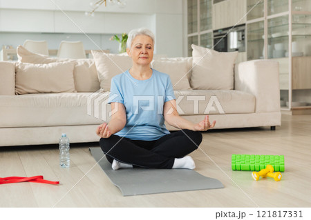 Yoga mindfulness meditation. Senior adult mature woman practicing yoga at home. Mid age old lady sitting in lotus pose on yoga mat meditating relaxing. Older middle aged woman doing breathing practice 121817331