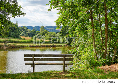 Relaxing lake or park bench to enjoy zen landscape view of scenic pond or bay of water in nature reserve or botanical garden. Local wooden seating or furniture in serene, tranquil or calm countryside 121818903