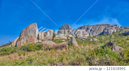 Landscape of rocky mountain with boulders against a blue sky in summer. Green field with rocks and wild grass growing on sunny day outside with copy space. Scenic remote travel destination in nature 121818991