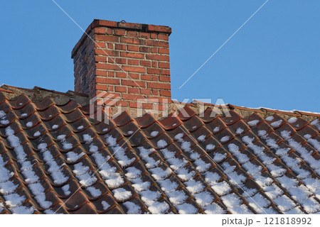 Red brick chimney designed on the roof of a snow covered residential house or building against a clear sky background. Air vent construction for the release of smoke and heat from fireplace in winter 121818992