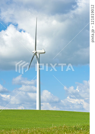 Windmill. A windmill on a green hill against cloudy blue sky with copy space. Wind turbines generate electricity through spinning propeller blades. Conceptual nature scene for renewable energy. 121819012