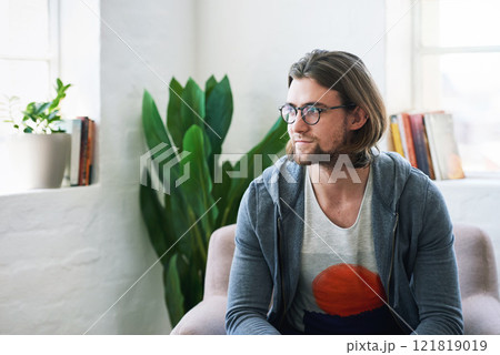 Young man looking out window thinking sitting on sofa at home 121819019
