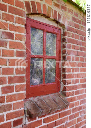 Old dirty window in a red brick house or home. Decaying casement with redwood frame on a historic building with clumpy paint texture. Exterior details of a windowsill in a traditional town or village 121819337
